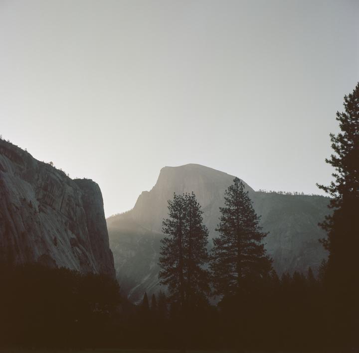 Sunlight illuminates a mountain peak behind silhouetted trees and a valley.