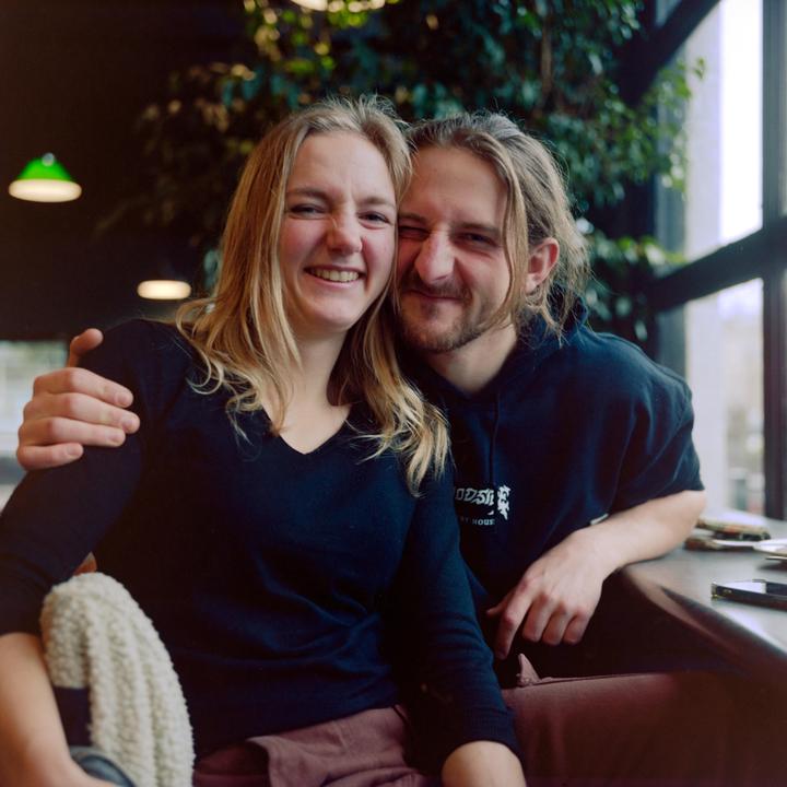 A couple sits close together at a table in a cafe, smiling at the viewer.