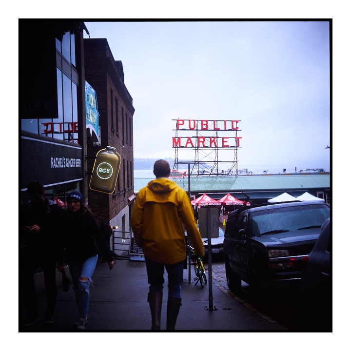 A man in a yellow raincoat walks along a street with a "Public Market" sign visible in the background.