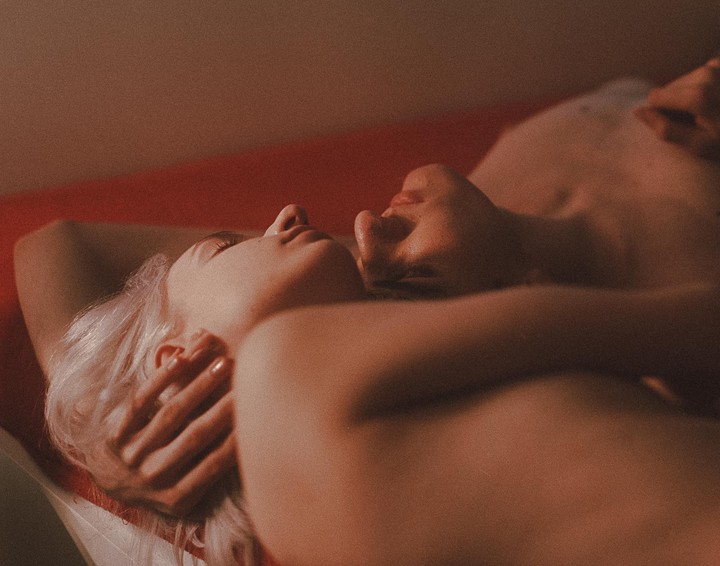A couple lies intimately on a red surface, bathed in warm, soft light.