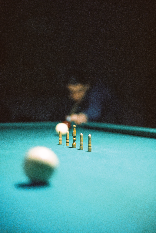 A man plays billiards with a cue ball in the foreground and wooden pins on the table.