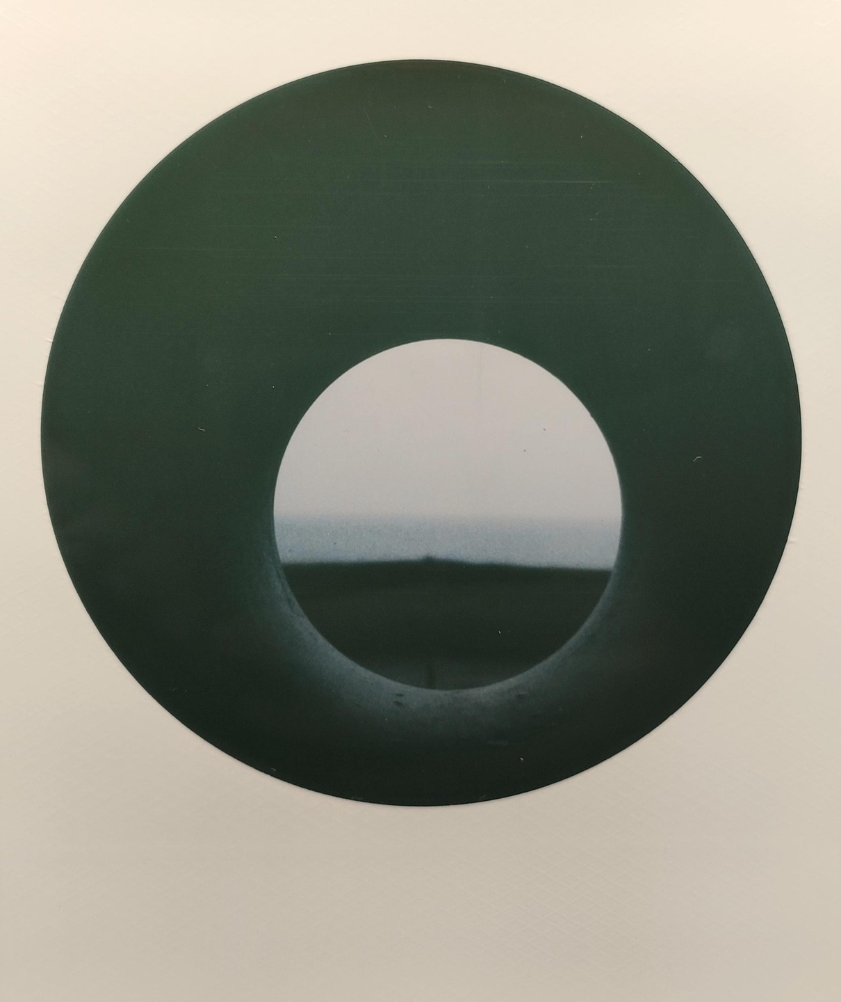 A dark green circle with a white center frames a distant horizon line under a hazy sky.