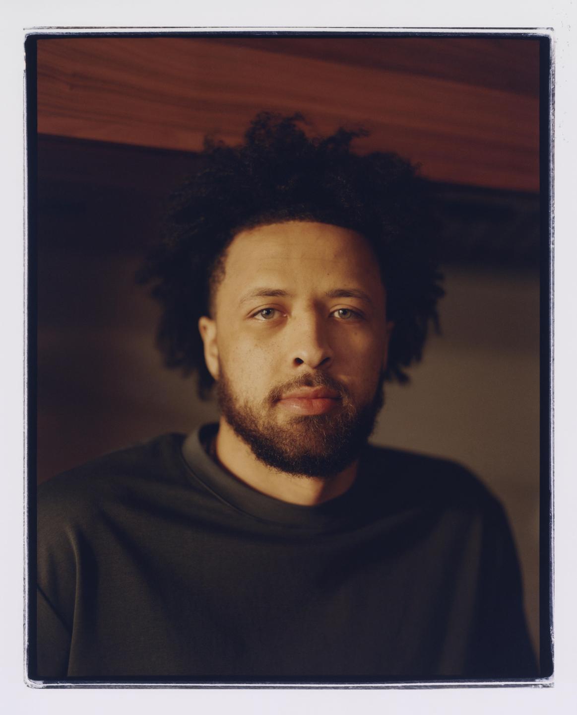 A man with curly hair and a beard looks directly at the viewer in a headshot.