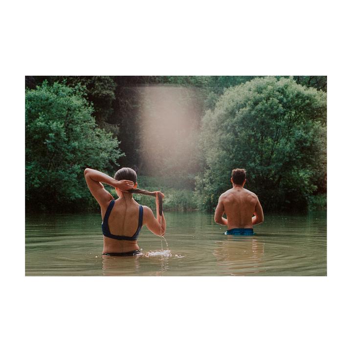 A woman and a man are standing in a body of water surrounded by trees.