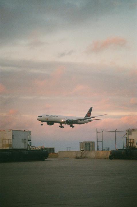An Air Canada airplane descends for landing against a pastel sky.