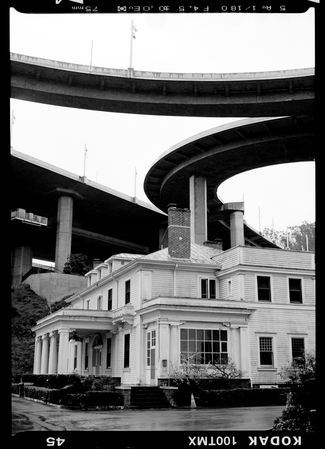 A large white house with columns stands beneath an elevated highway overpass.