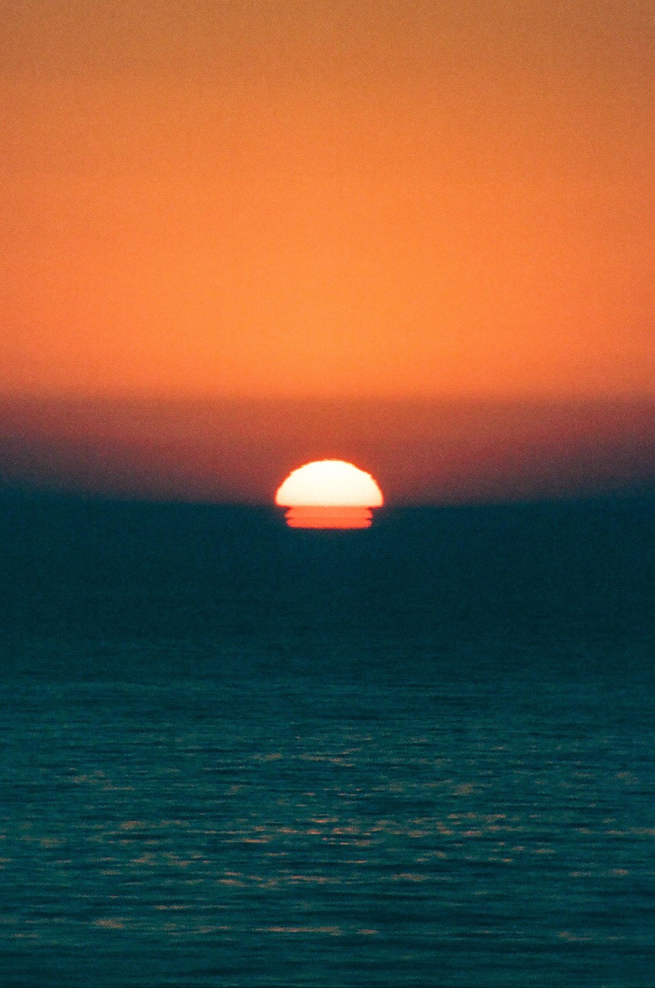 The sun sets over the ocean, creating a vibrant orange and blue sky.