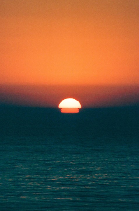 The sun sets over the ocean, creating a vibrant orange and blue sky.