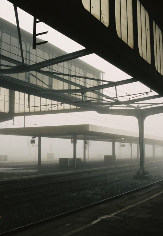 A train station platform and tracks are visible through a thick fog.