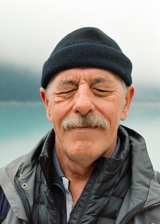 A man with a mustache and a black beanie squints with his eyes closed against a bright background.