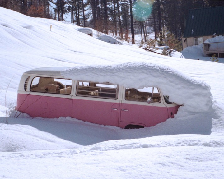 A pink and white van is buried in deep snow on a sunny winter day.