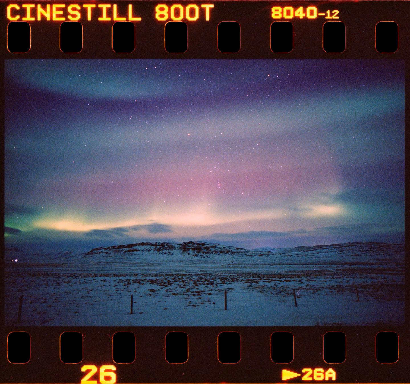 The aurora borealis glows above a snowy landscape with a fence in the foreground.