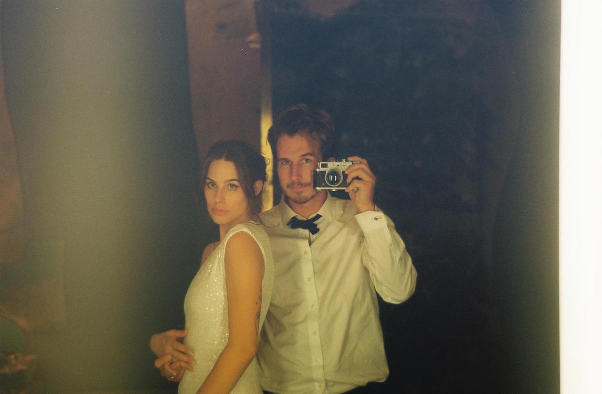 A man and a woman pose for a self-portrait in a mirror, with the man holding a camera to his face.