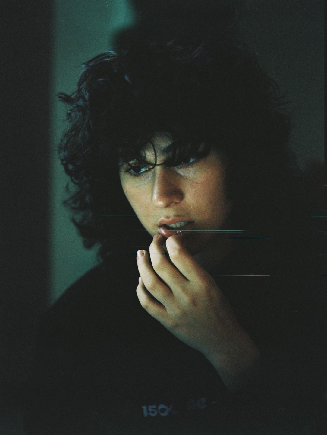 A woman with dark, curly hair looks down with her fingers near her mouth.