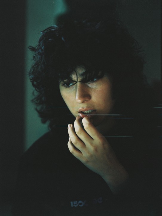 A woman with dark, curly hair looks down with her fingers near her mouth.
