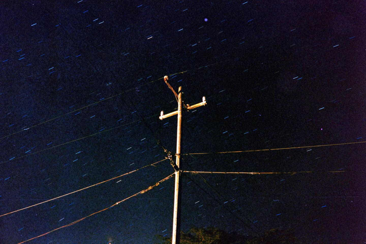 A utility pole and power lines are visible against a night sky filled with star trails.