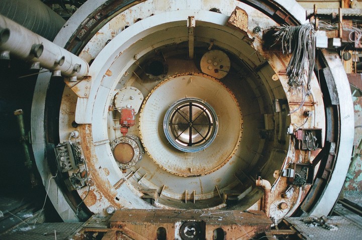 A large, circular, rusty industrial machine with a central grate is shown in a close-up.