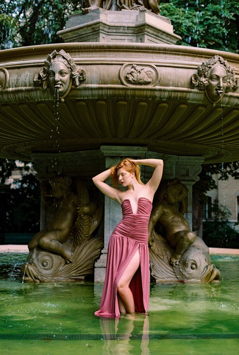 A woman in a pink dress stands in a fountain with water up to her knees.