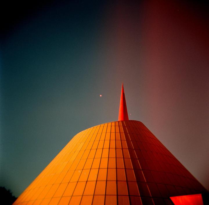 A conical building with a red spire is visible against a gradient sky.