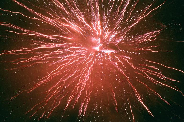 A red firework explodes in the night sky, creating streaks of light.