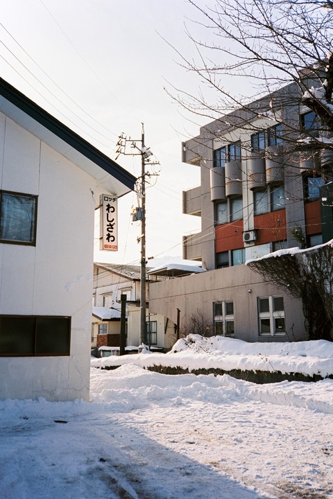 A snow-covered street with buildings and utility poles under a bright sky.