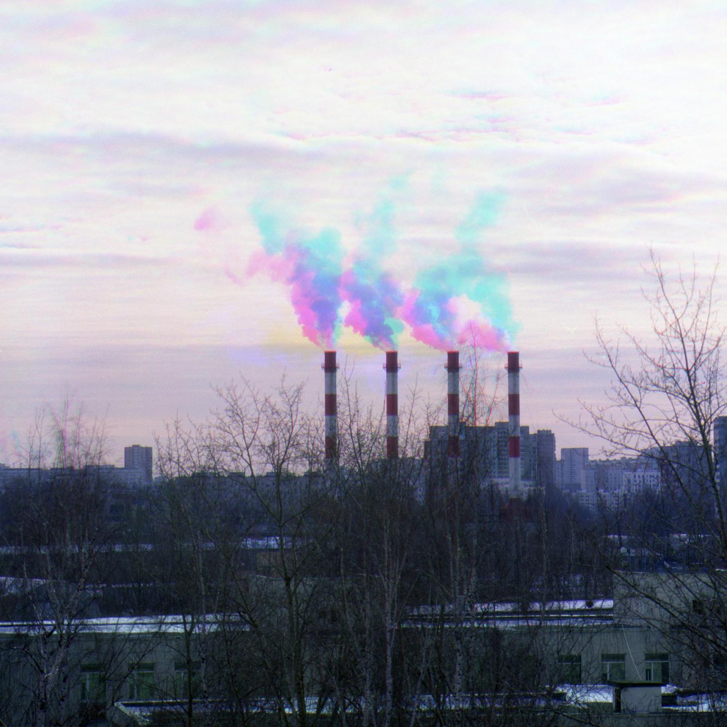 Four red and white striped smokestacks emit colorful smoke into a cloudy sky above a city.