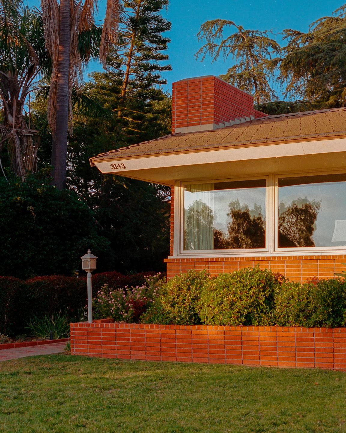 A brick house with large windows and a well-maintained garden is bathed in golden hour light.