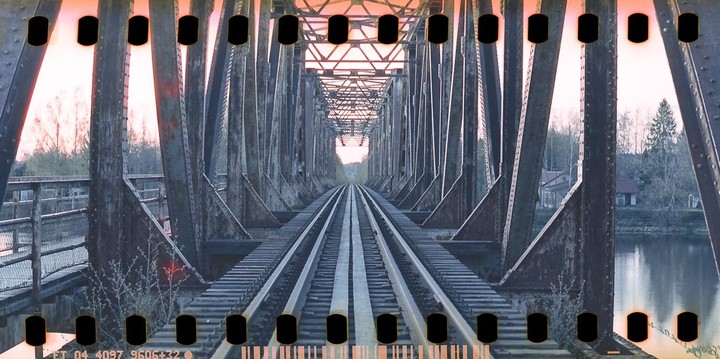 A long railway bridge stretches over a body of water, with trees and buildings visible on the far bank.