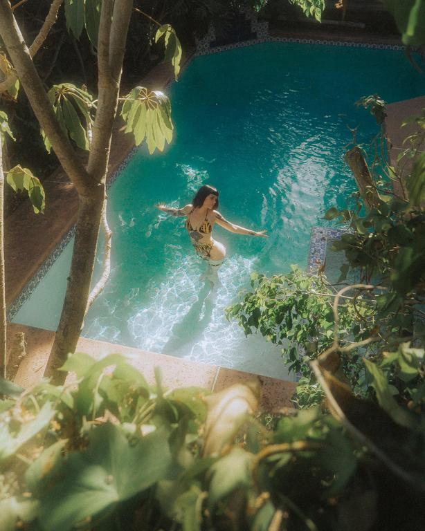 A woman in a patterned swimsuit floats in a swimming pool surrounded by lush green foliage.