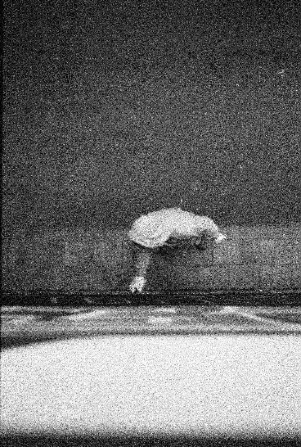 A person in a light-colored hoodie walks on a sidewalk next to a street, viewed from above.