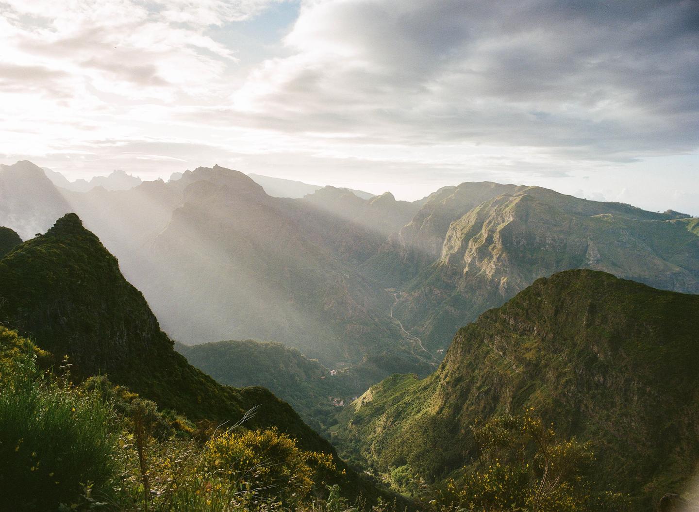 Sunlight streams through clouds over a lush green mountain valley.