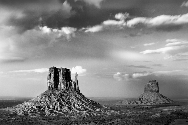 Two large rock formations stand in a desert landscape under a cloudy sky.