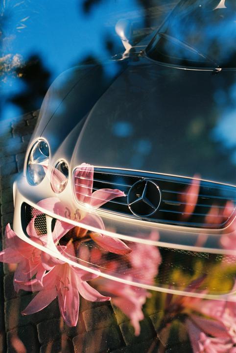 A double exposure shows the front of a car with a Mercedes-Benz emblem overlaid with pink flowers.