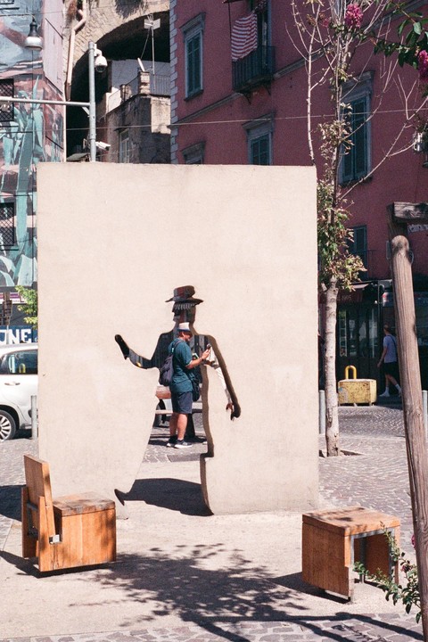 A man stands inside a cutout of a cartoon figure in a wall on a street.