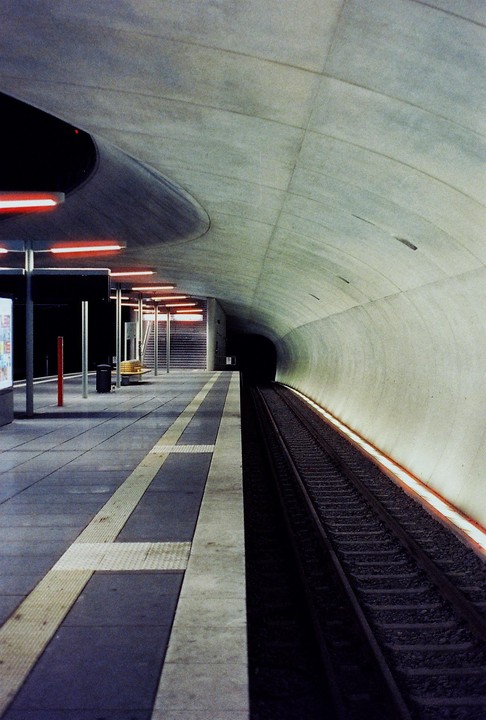 A subway platform with red lights on the left and a dark tunnel on the right.