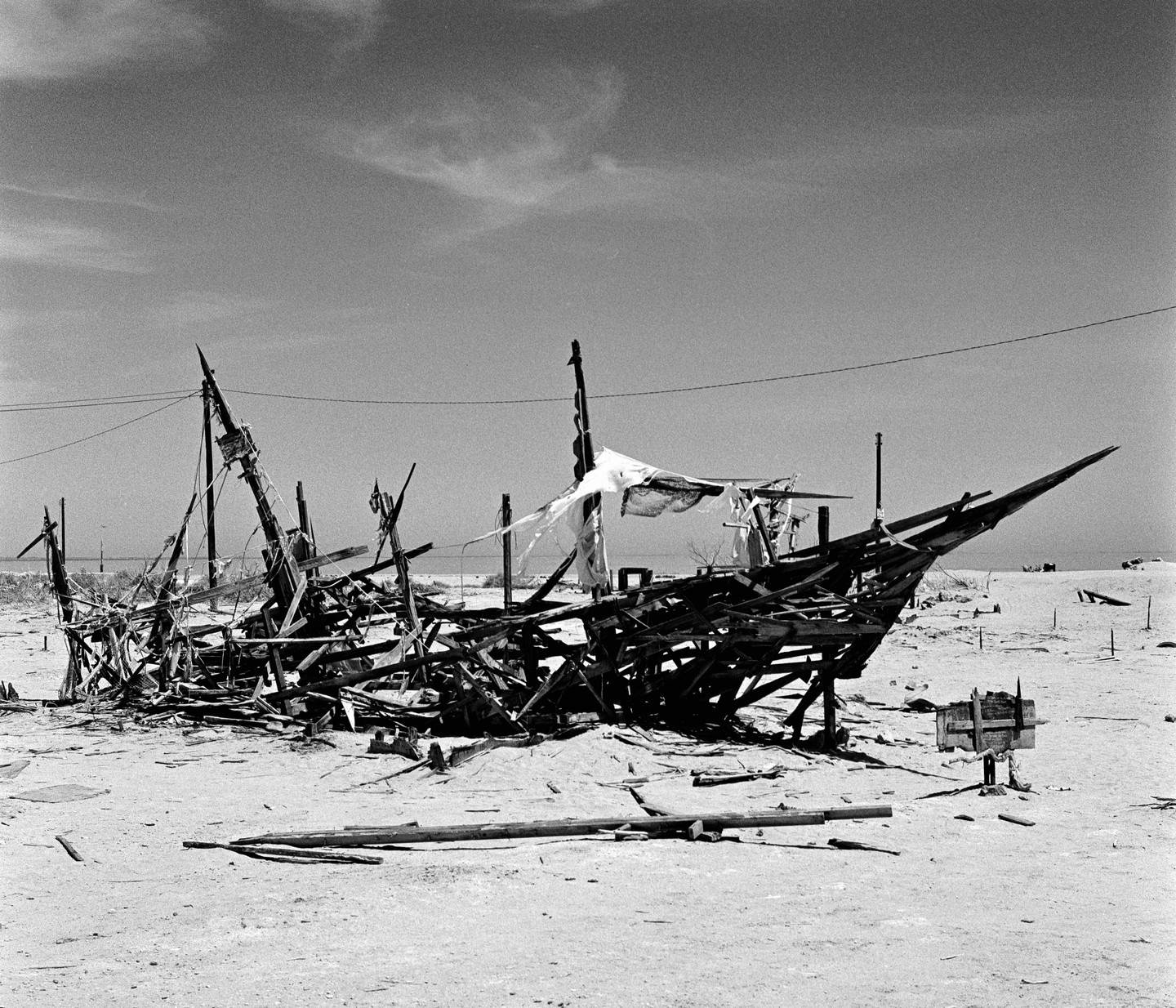 A derelict wooden boat lies broken on a sandy shore under a bright sky.