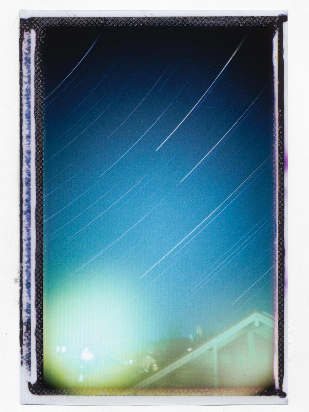 A long exposure photograph captures star trails across a blue night sky above a building.