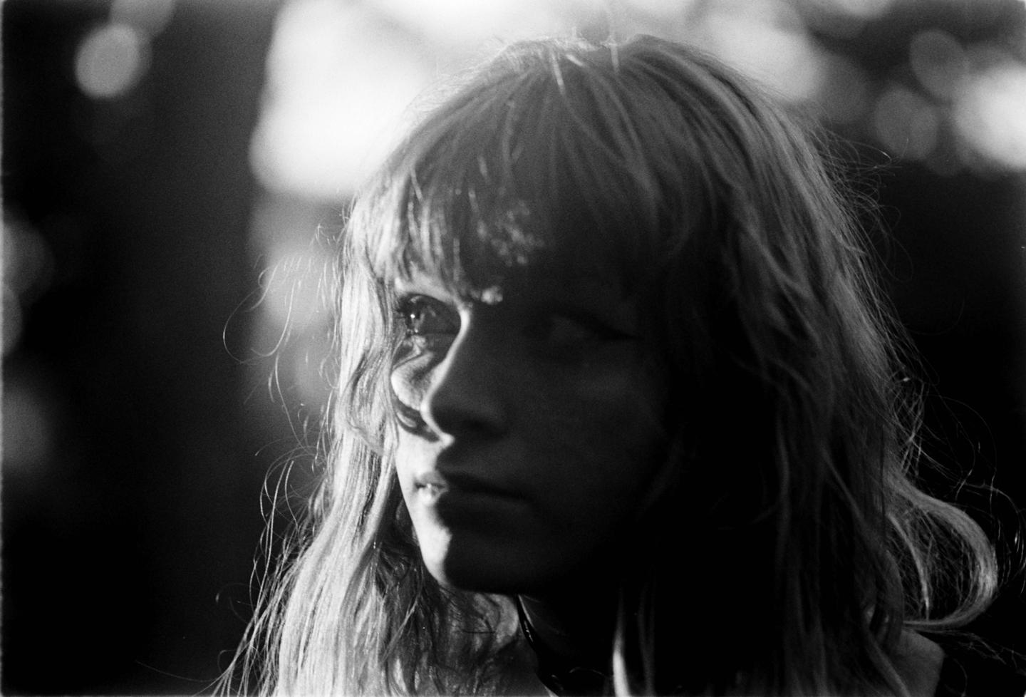A woman with long hair is illuminated by light from the side, creating strong shadows on her face.