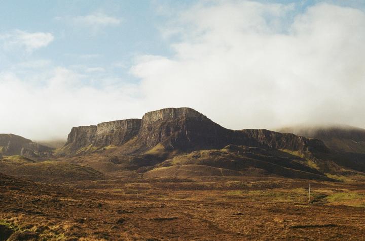 A vast, rugged landscape features a large mountain range under a cloudy sky.