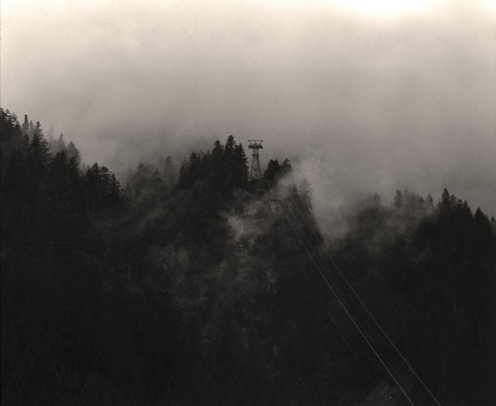 A cable car tower stands on a forested mountain shrouded in fog.