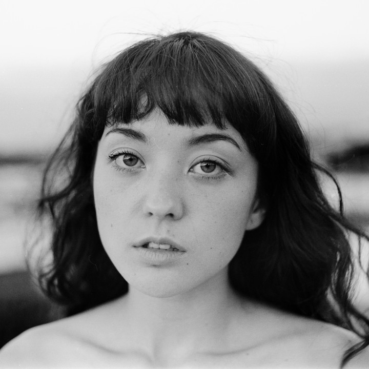 A woman with bangs and dark hair looks directly at the viewer.