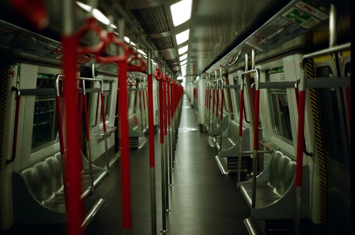 The interior of an empty subway car is visible, with rows of red handrails and seats on either side.