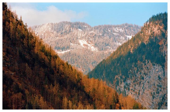 Three mountains with different vegetation stages are visible under a blue sky.