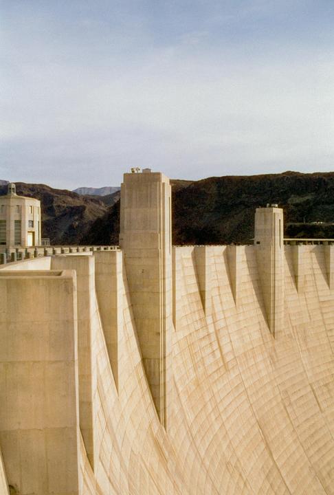 The Hoover Dam is visible with mountains in the background under a cloudy sky.