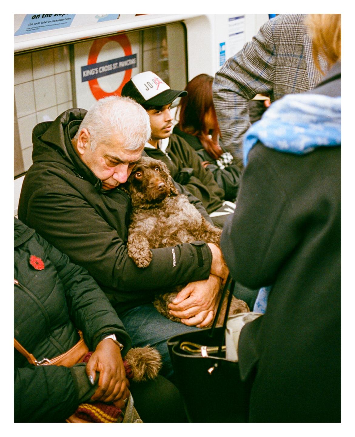 A man sleeps with a dog in his arms on a subway train.