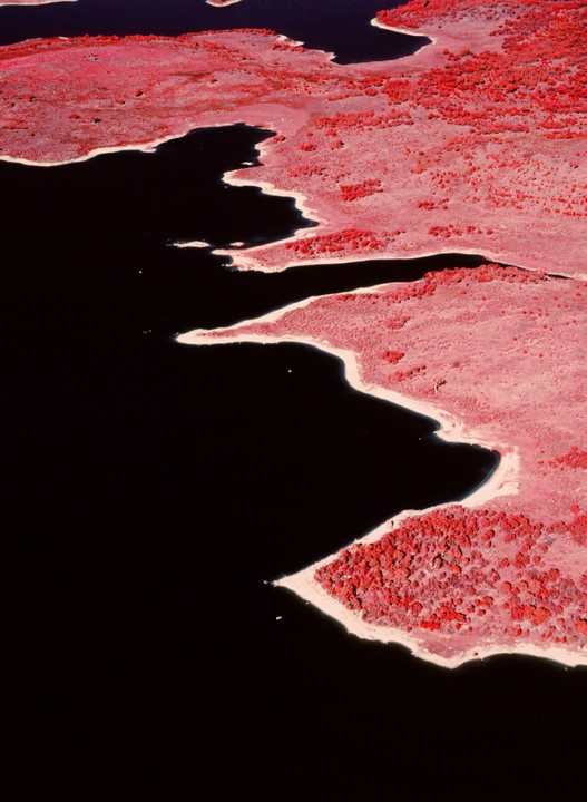 An aerial view shows the dark water of Lake Jindabyne next to a shoreline with red foliage.