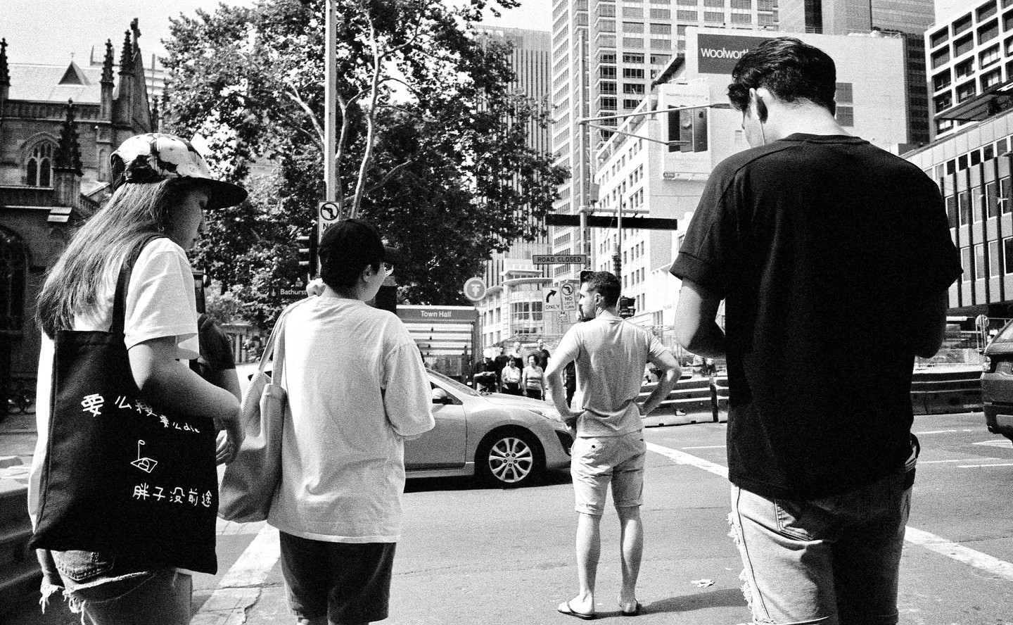Four people stand on a city street with buildings and trees in the background.