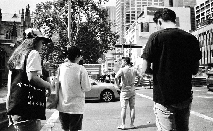 Four people stand on a city street with buildings and trees in the background.