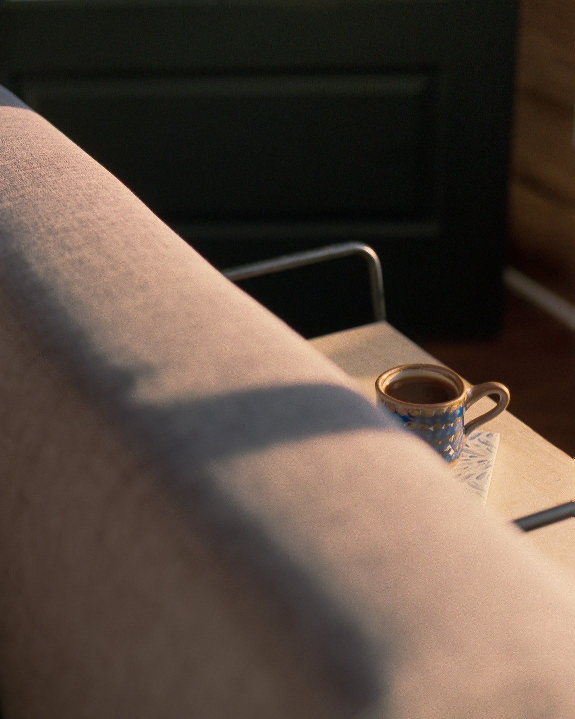 A patterned mug filled with a beverage sits on a coaster on a wooden surface, partially obscured by a light-colored fabric.