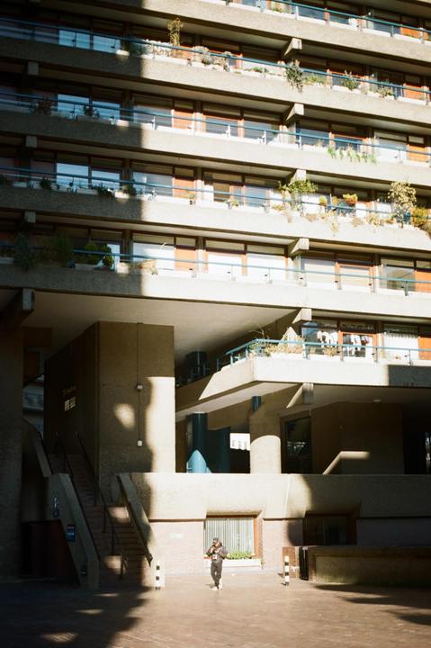 A person walks on a paved area in front of a large concrete building with many balconies and windows.